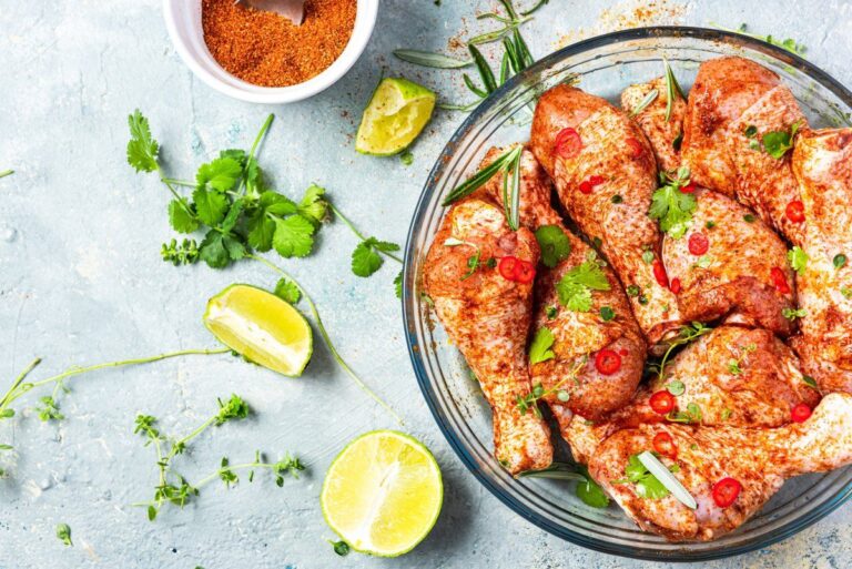 Pilons de poulet crus marinant dans un plat avec épices, herbes et piment.