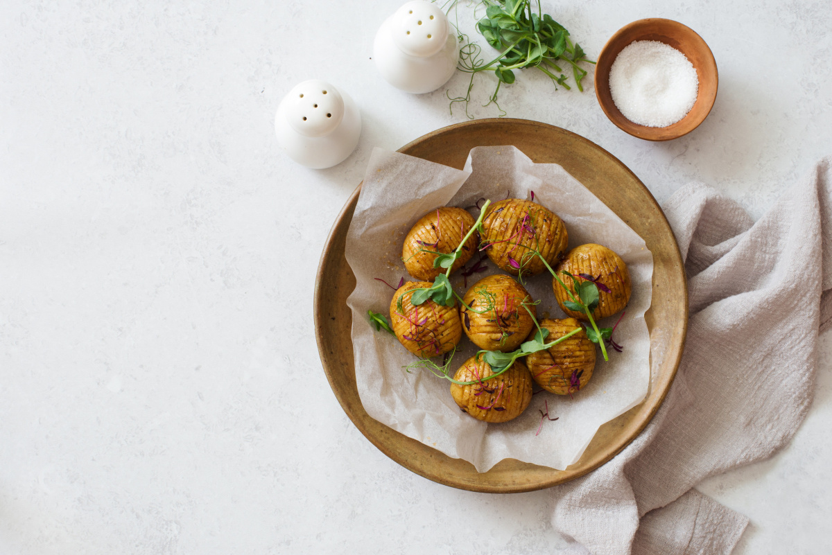 Pommes de terre Hasselback dor&eacute;es au four, garnies de jeunes pousses fra&icirc;ches.