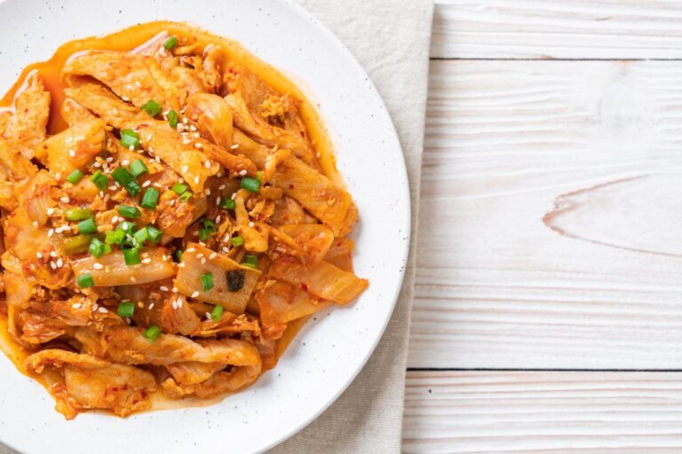 Plat de porc sauté au kimchi épicé, garni de ciboule et graines de sésame.