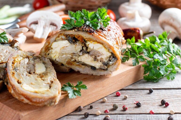 Roulé de porc rôti aux champignons et fromage, tranché sur une planche en bois.