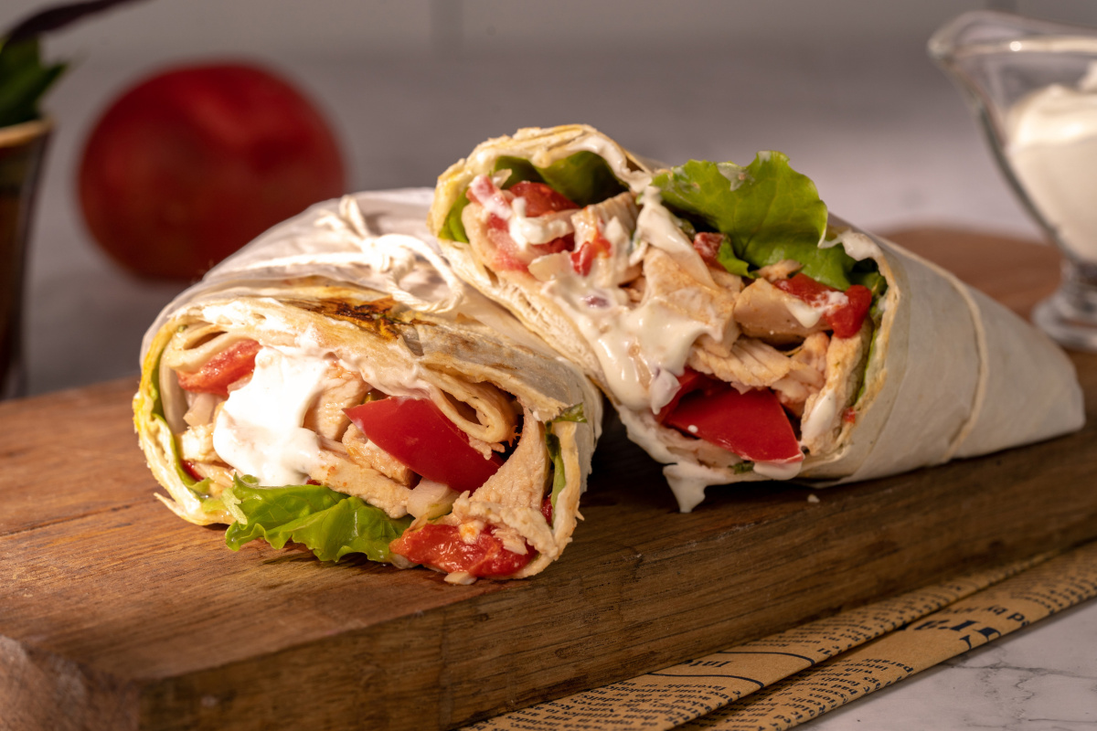 Shawarma au poulet et l&eacute;gumes coup&eacute; en deux garni de sauce blanche.