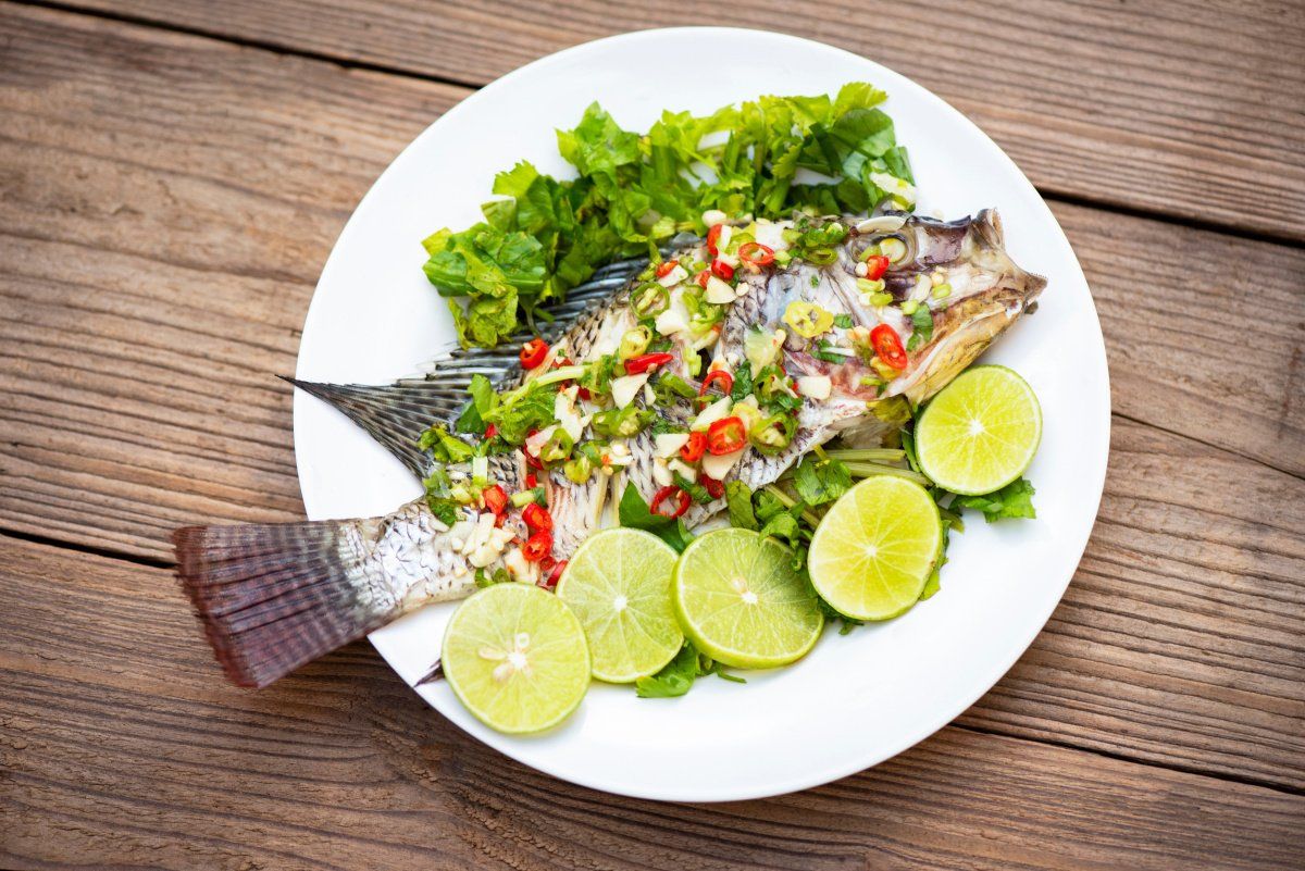 Poisson tilapia entier &agrave; la vapeur garni de piment, ail et tranches de citron vert.