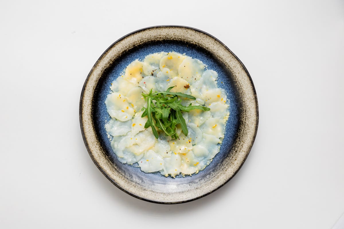 Carpaccio de fruits de mer en fines tranches, assaisonn&eacute; et garni de roquette.