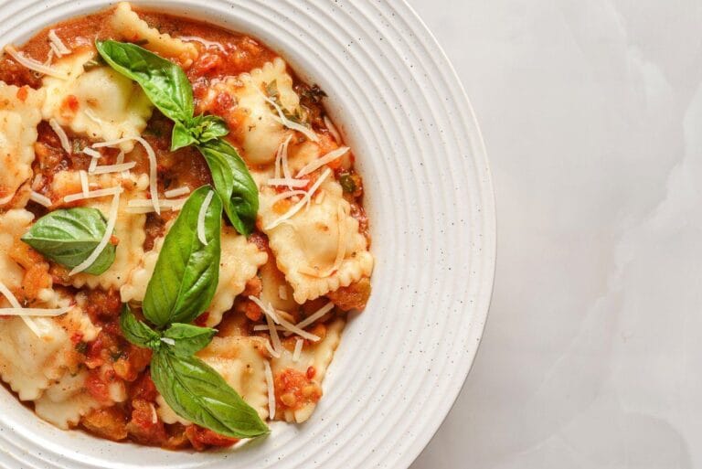 Raviolis à la sauce tomate, garnis de basilic frais et de fromage rapé.