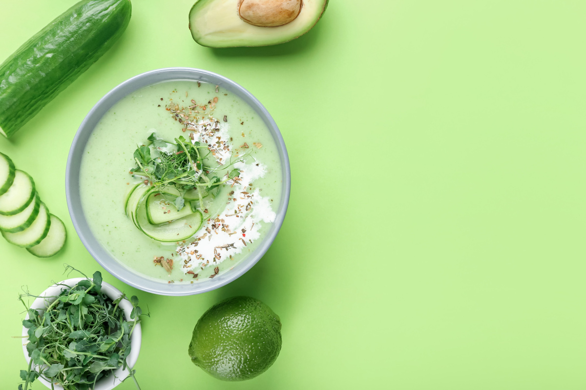 Bol de soupe froide vert au concombre et avocat, garni de micropousses et de cr&eacute;me